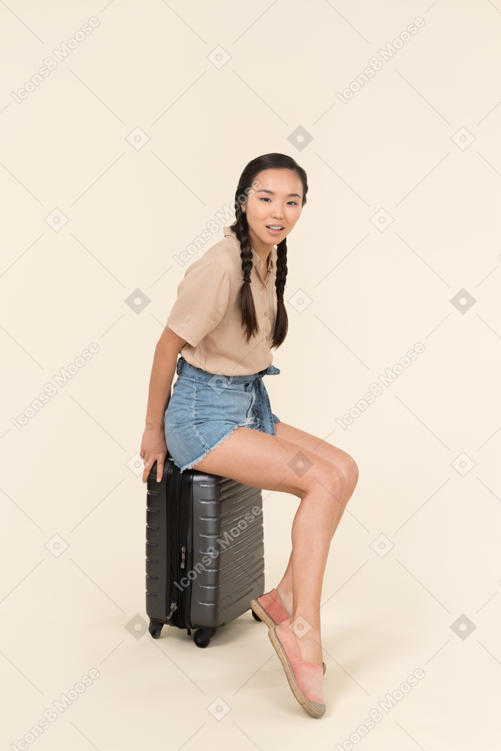 Young female traveller sitting on suitcase and looking involved in her thoughts