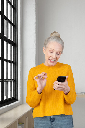 An older woman holding a cell phone in front of a window