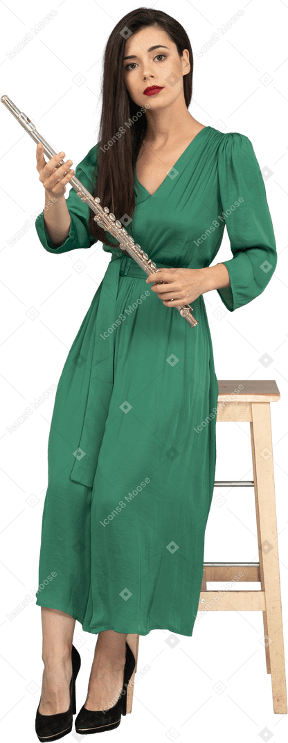 Vorderansicht einer jungen dame im grünen kleid, die auf einem stuhl sitzt und klarinette hält
