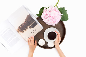 Cup of coffee, meringues, white flower and book on round wooden tray