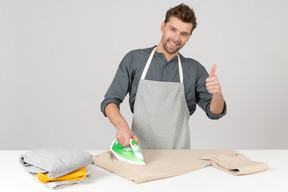 Handsome young guy ironing and showing thumb up