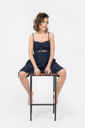 Displeased woman sitting on bar stool with her legs spread apart
