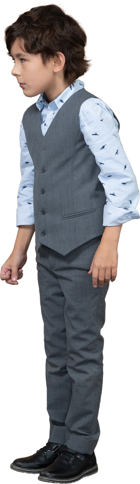 Vista lateral de un chico lindo con traje gris mirando algo con interés
