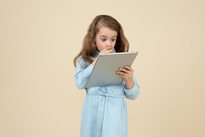 Mignonne petite fille en regardant l'écran de sa tablette avec un regard surpris