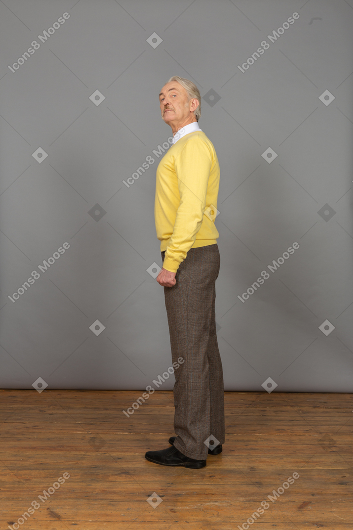 Вид сбоку на пожилого любопытного человека в желтом свитере, поднимающего голову и смотрящего в камеру