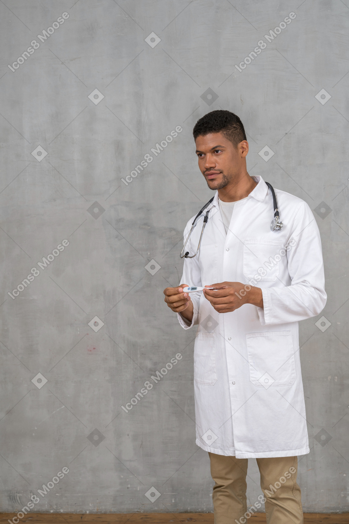 Médico varón sosteniendo un termómetro