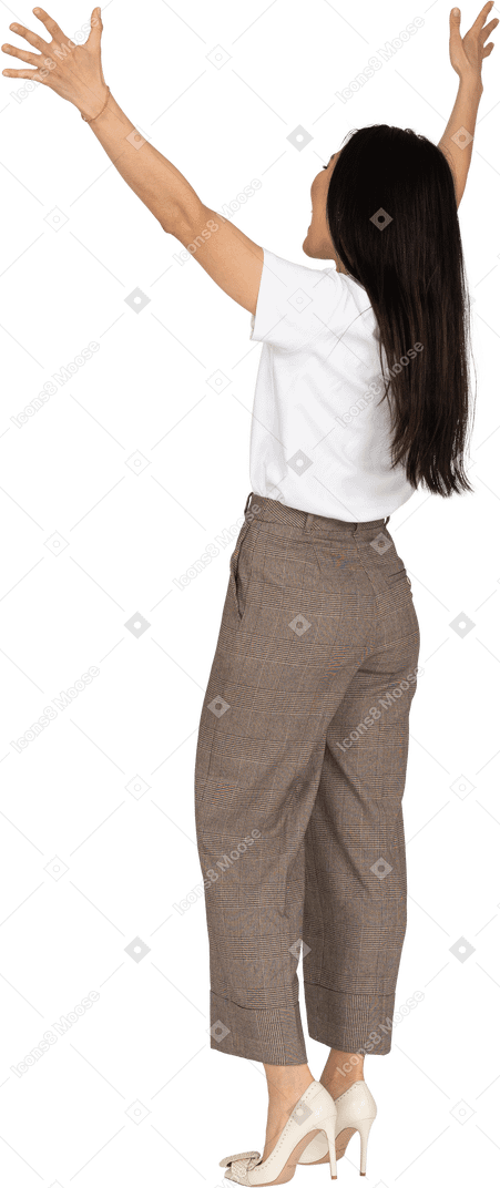 Vista posteriore di tre quarti di una giovane donna felice in calzoni e maglietta alzando le mani