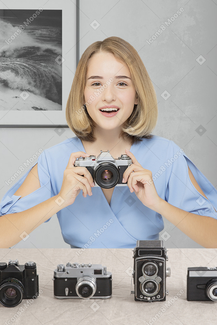 テーブルの上にレトロなカメラを持って座っている笑顔の若い女性