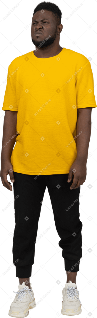 노란색 티셔츠를 입은 불쾌한 얼굴을 찡그린 젊은 검은 피부의 남자의 전면 모습