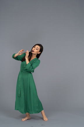 Three-quarter view of a young lady in green dress playing flute while leaning back