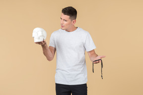 Young guy holding skull in one hand and looking at prayer beads he's holding in another hand