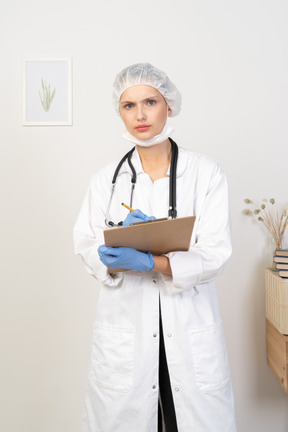 Vista frontal de una joven doctora perpleja tomando notas en su tableta