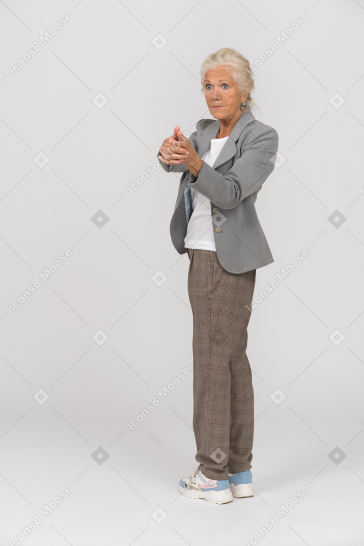 Vue latérale d'une vieille dame en costume montrant un pistolet avec les doigts