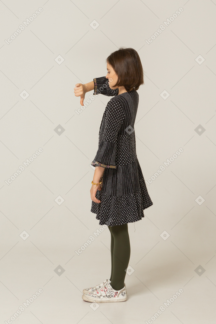 Vista laterale di una bambina dispiaciuta in abito che mostra il pollice verso il basso