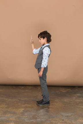 Vista lateral de un niño con traje gris que muestra el signo de ok