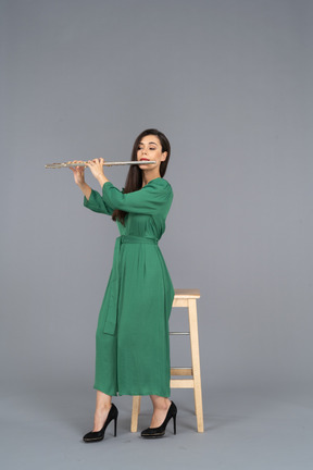 Figura intera di una giovane donna in abito verde seduta su una sedia mentre suona il clarinetto