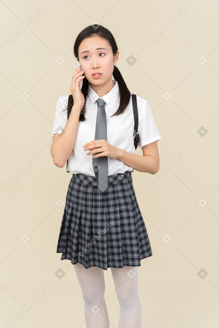 Menina da escola asiática ouvindo atentamente o que é dito no telefone
