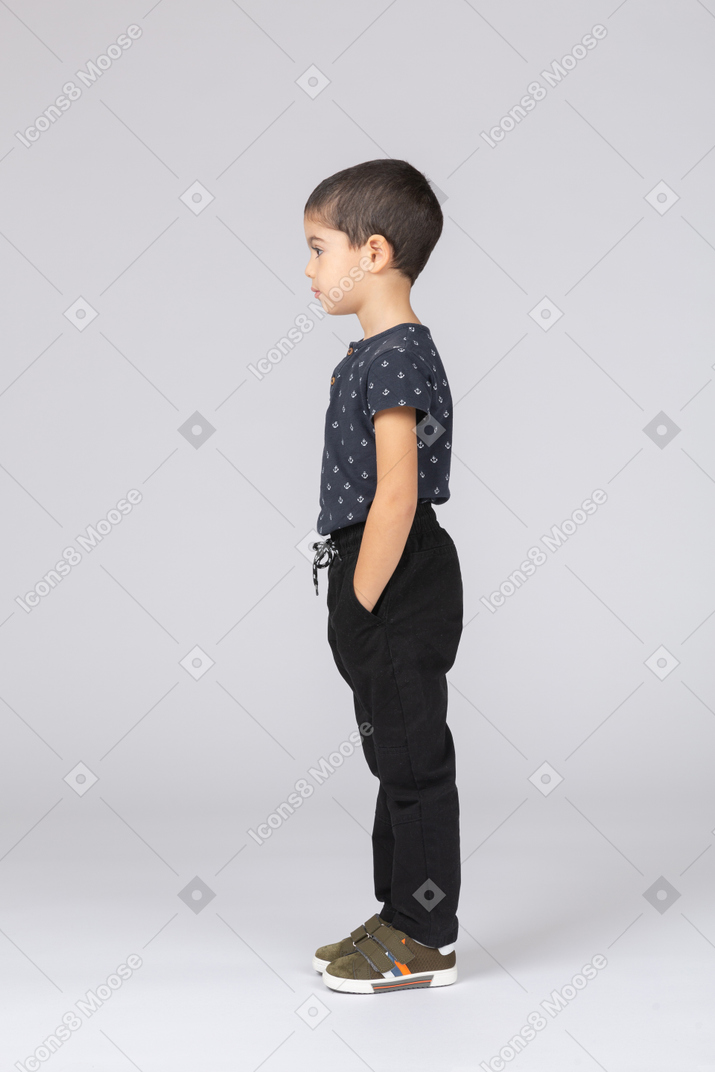 Side view of a cute boy in casual clothes posing with hands in pockets