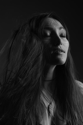 Noir three-quarter portrait of a young female with ethnic facial art and messy hair closing her eyes