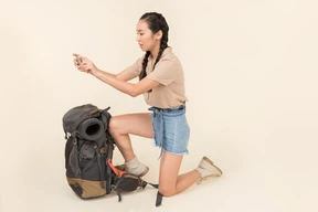 Joven mujer asiática de pie cerca de la mochila y tomar fotos