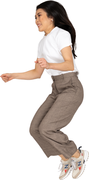Vista di tre quarti di una giovane donna che salta in calzoni e t-shirt piegando le ginocchia