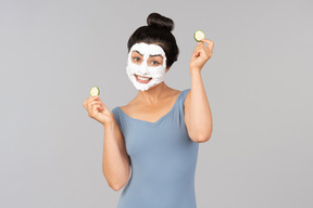 Jeune femme avec un masque facial blanc sur la tenue de tranches de concombre