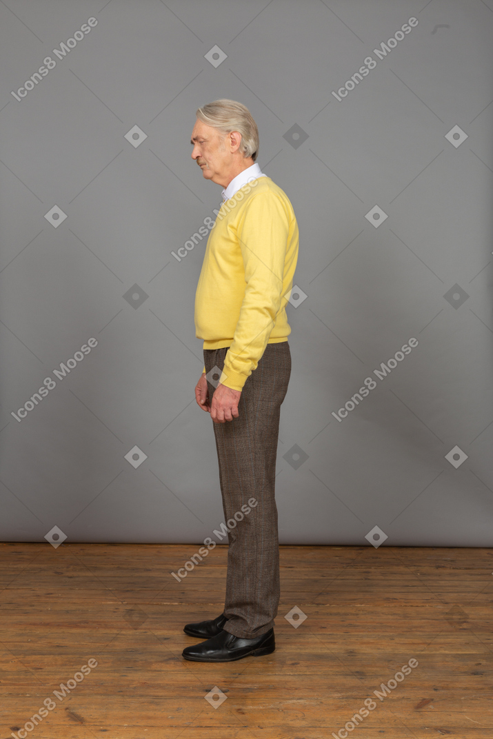 Vue latérale d'un vieil homme triste en pull jaune debout toujours avec les yeux fermés