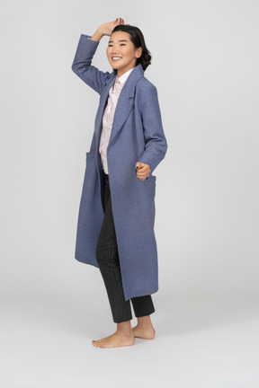 Cheerful woman in coat standing with hand up