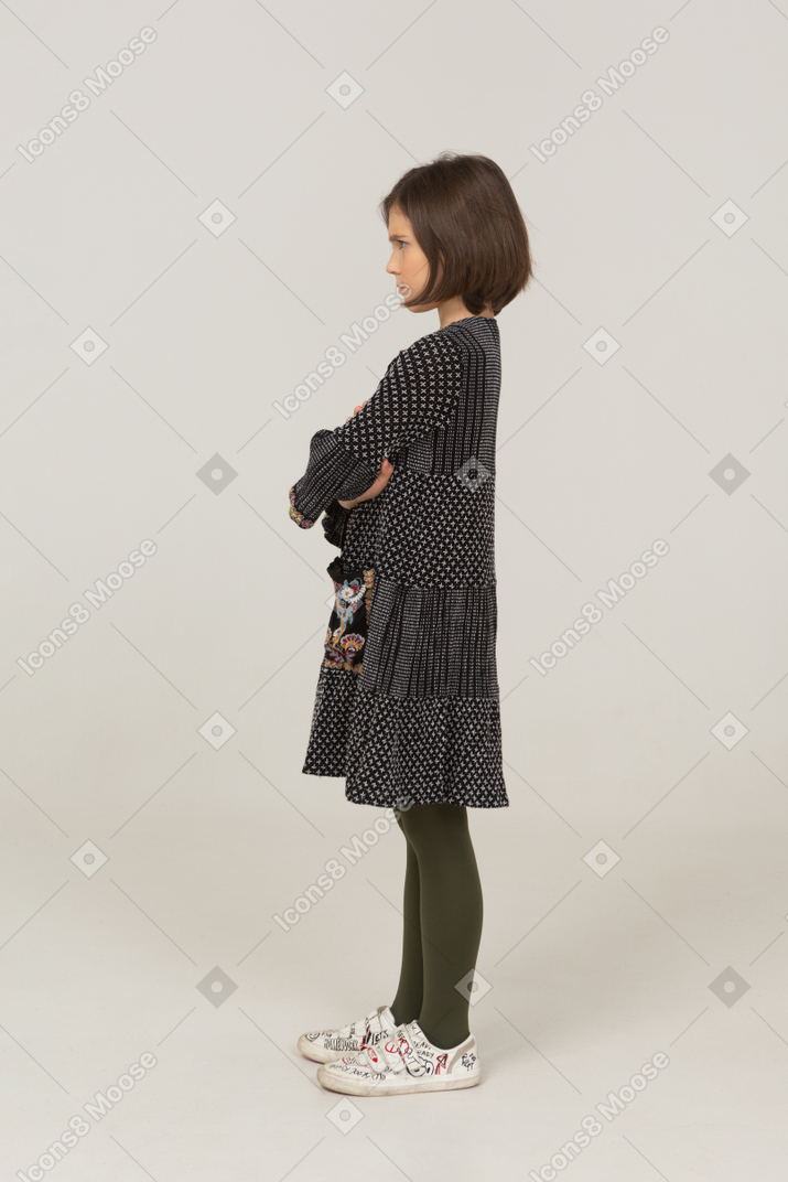Vista laterale di una bambina offesa in abito che incrocia le braccia