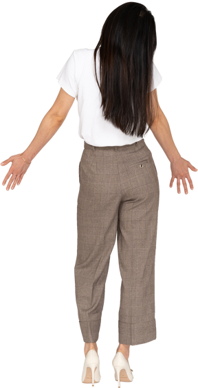Vista posteriore di una giovane donna in calzoni e t-shirt allargando le mani