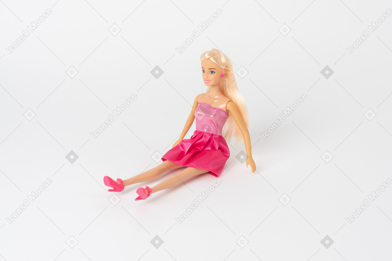 A beautiful barbie doll in a shiny pink dress and pink high heels sitting isolated against a plain white background