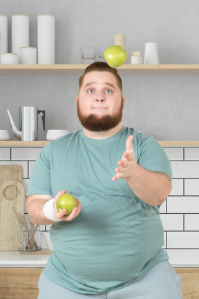 A man juggling apples in kitchen