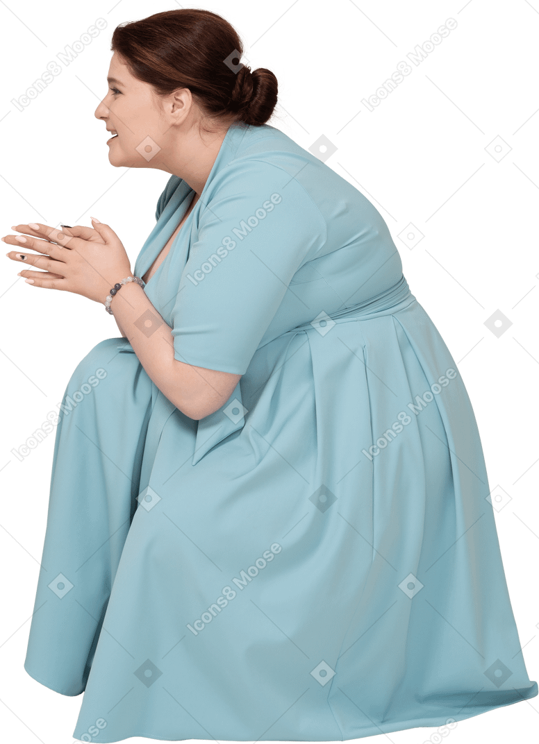 Женщина в синем платье сидит на корточках, вид сбоку