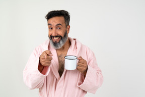 Homme d'âge mûr positif pointant avec le doigt et tenant une tasse