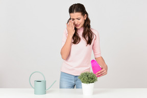 Attractive young woman wiping her eyes while taking care of a houseplant