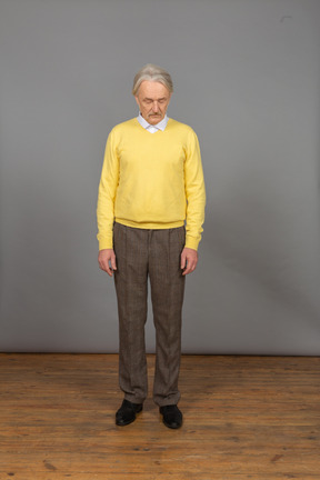 Vista frontal de um homem velho e triste em um pulôver amarelo se curvando com os olhos fechados