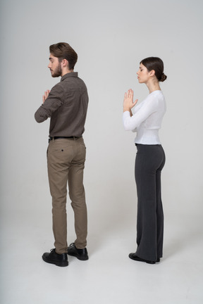 Three-quarter back view of a praying young couple in office clothing holding hands together