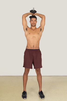 A frontal view of the handsome athletic man doing exercises with the dumbbell and looking to the camera
