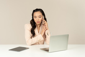 Oficinista asiática hablando por teléfono y trabajando en la computadora portátil