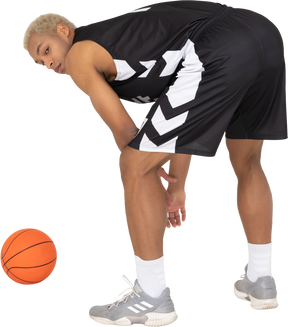 Three-quarter back view of a young male basketball player standing by the ball