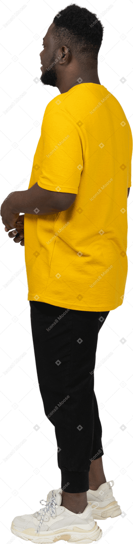 Vista posteriore di tre quarti di un giovane uomo dalla pelle scura in maglietta gialla che si tiene per mano insieme