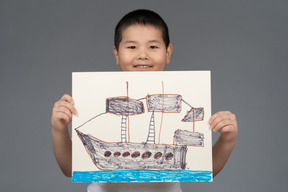 Smiling asian boy showing a drawing of a ship