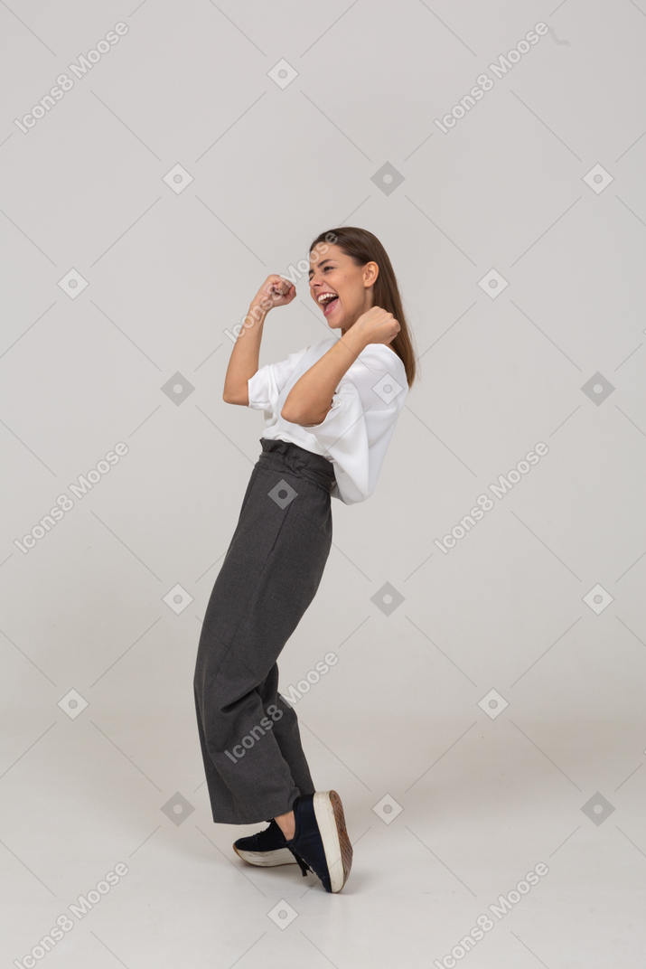 Three-quarter view of a happy young lady in office clothing raising hands