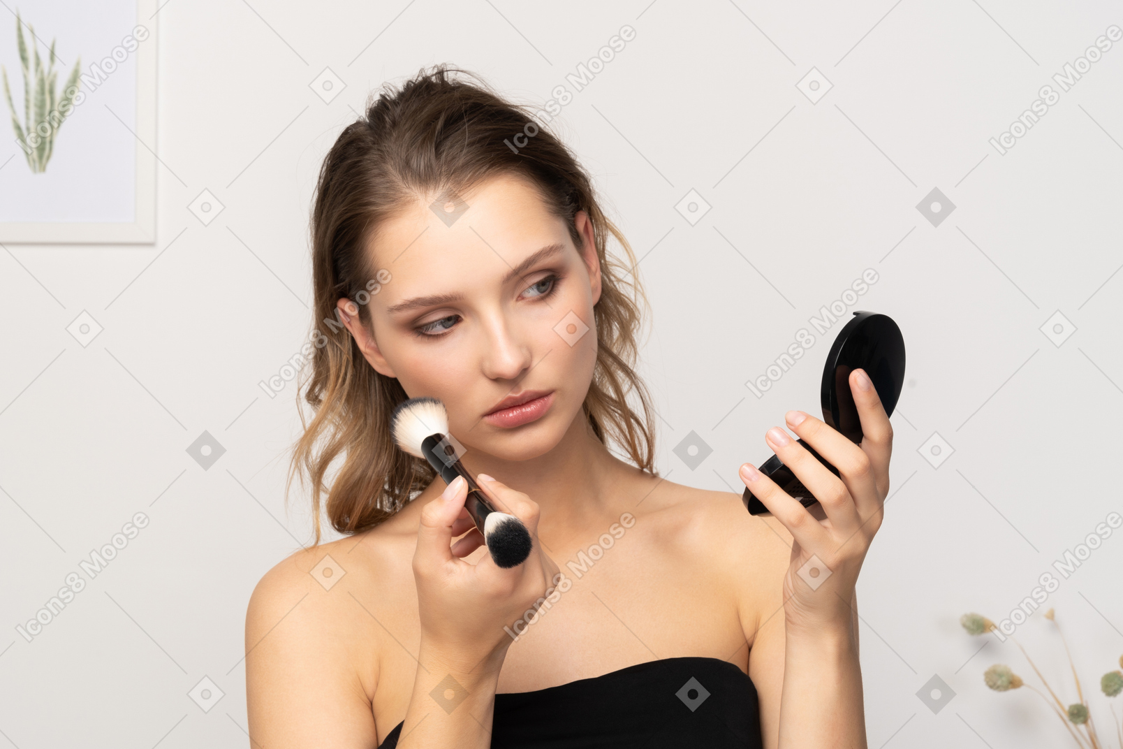 Vista frontal de uma jovem aplicando pó facial enquanto segura um espelho