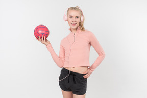Joven rubia en traje negro y rosa posando con artículos deportivos sobre un fondo gris claro