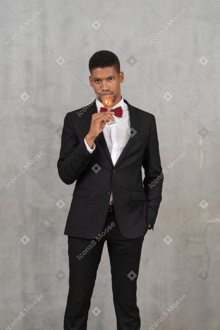 Young man drinking from a flute glass and looking at camera