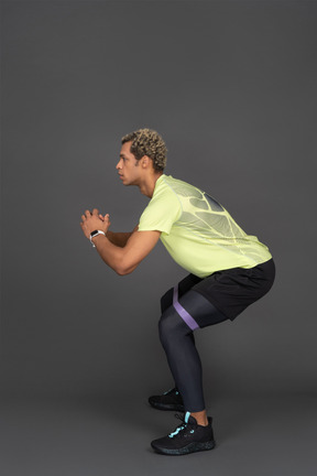 Side view of a dark-skinned young man squatting with an elastic rubber