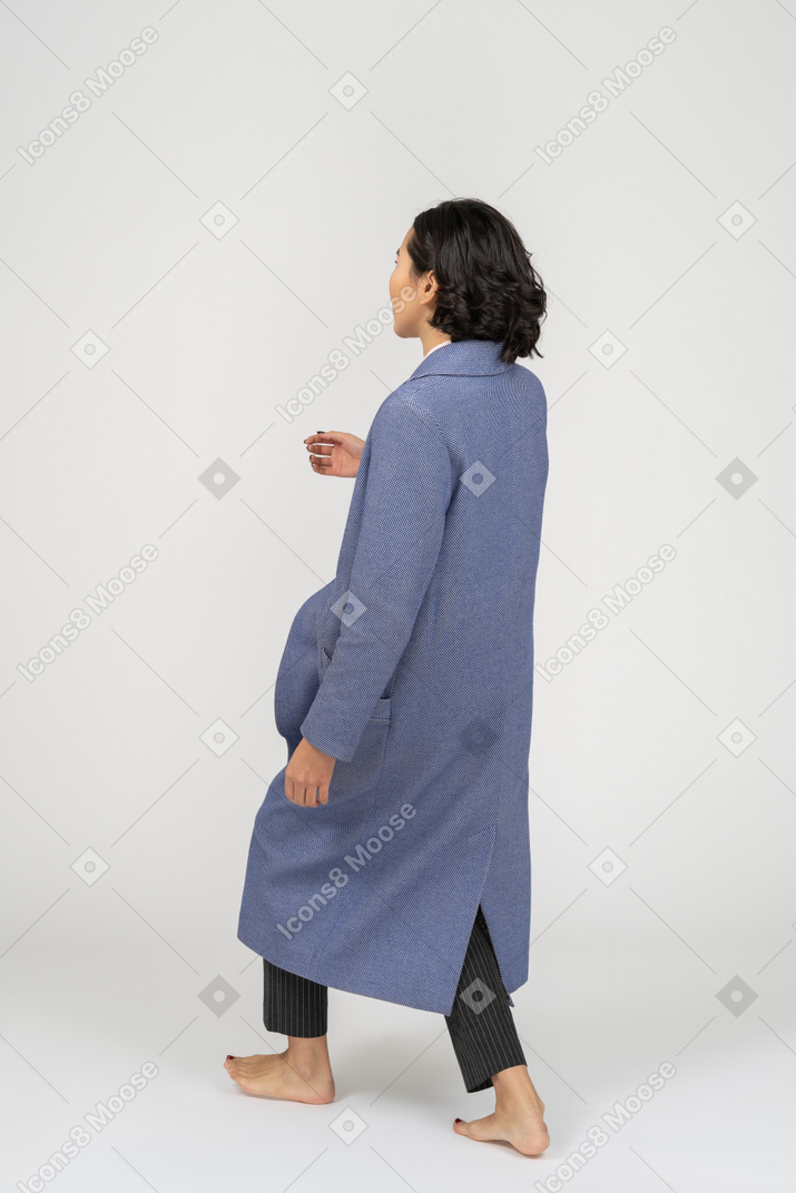Vista lateral de la mujer con abrigo caminando e inclinándose hacia atrás