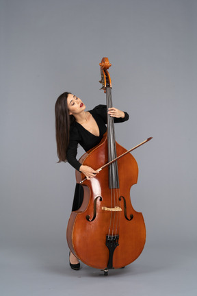 Front view of a young woman in black dress playing the double-bass with a bow while leaning back