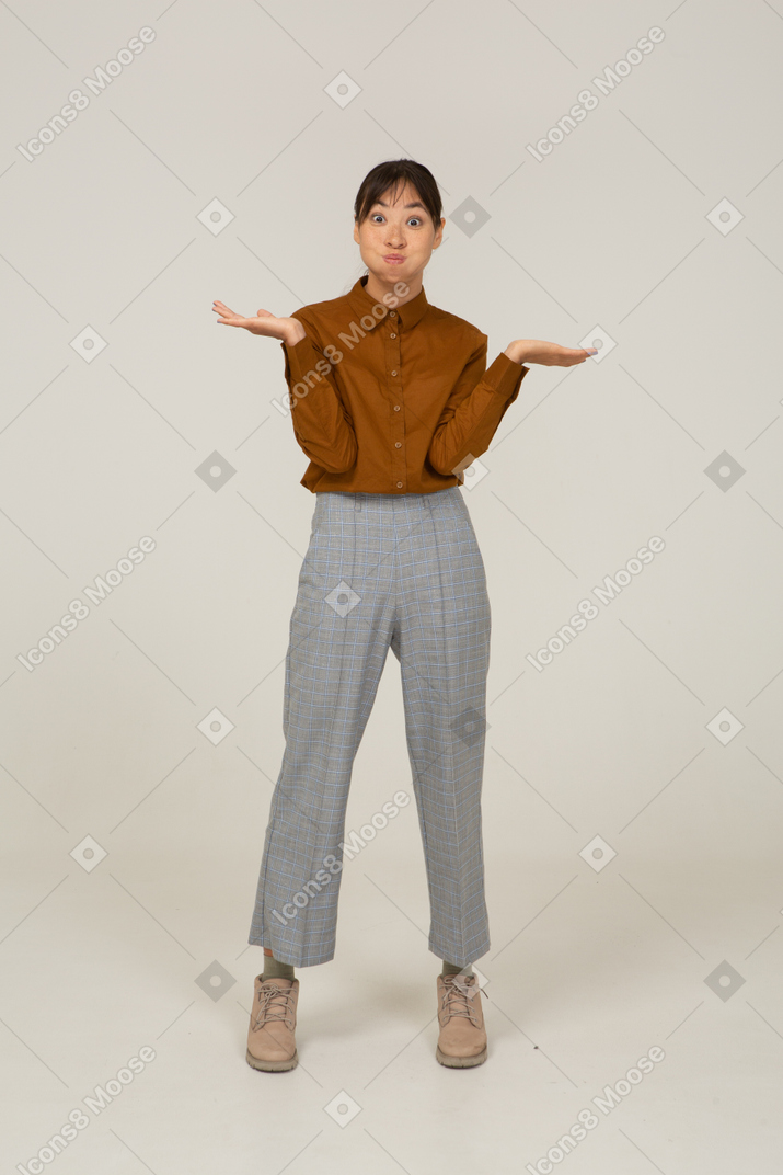 Vista frontale di una divertente giovane donna asiatica in calzoni e camicetta che alza le mani